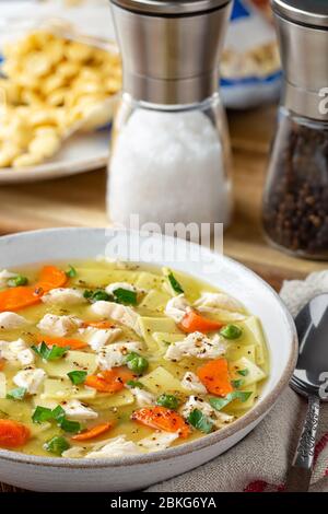 Schüssel mit Hühnernudel und Gemüsesuppe Suppe mit Salz, Pfeffer und Cracker im Hintergrund Stockfoto