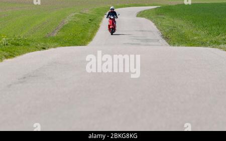 Kiel, Deutschland. Mai 2020. Bei sonnigem Wetter fährt eine Frau mit ihrem roten 125 ccm Vespa Roller auf einer unbefestigten Straße mit Schutzkleidung, Helm und Handschuhen. Seit 01.01.2020 brauchen Inhaber eines Autoführerscheins keinen separaten Motorradführerschein mehr. Nur 5 Fahrstunden und 4 Theoriestunden reichen aus, um Zweiräder bis zu 125 ccm fahren zu dürfen. Quelle: Axel Heimken/dpa/Alamy Live News Stockfoto