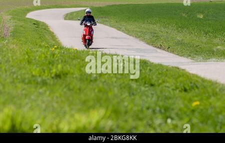 Kiel, Deutschland. Mai 2020. Bei sonnigem Wetter fährt eine Frau mit ihrem roten 125 ccm Vespa Roller auf einer unbefestigten Straße mit Schutzkleidung, Helm und Handschuhen. Seit 01.01.2020 brauchen Inhaber eines Autoführerscheins keinen separaten Motorradführerschein mehr. Nur 5 Fahrstunden und 4 Theoriestunden reichen aus, um Zweiräder bis zu 125 ccm fahren zu dürfen. Quelle: Axel Heimken/dpa/Alamy Live News Stockfoto