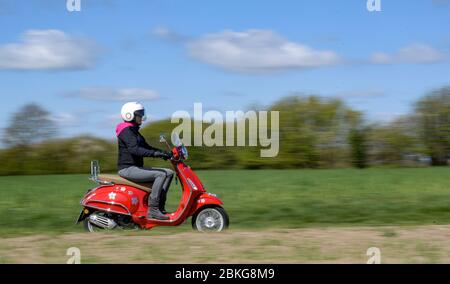 Kiel, Deutschland. Mai 2020. Bei sonnigem Wetter fährt eine Frau mit ihrem roten 125 ccm Vespa Roller auf einer unbefestigten Straße mit Schutzkleidung, Helm und Handschuhen. Seit 01.01.2020 brauchen Inhaber eines Autoführerscheins keinen separaten Motorradführerschein mehr. Nur 5 Fahrstunden und 4 Theoriestunden reichen aus, um Zweiräder bis zu 125 ccm fahren zu dürfen. Quelle: Axel Heimken/dpa/Alamy Live News Stockfoto