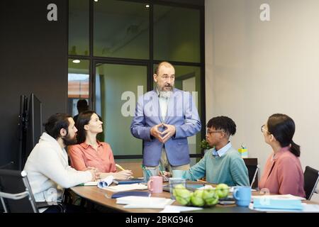 Senior Geschäftsmann steht vor seinen Kollegen im Vorstandszimmer und teilt seine Ideen, Kopierraum Stockfoto