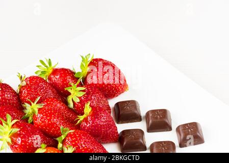 Erdbeeren und Stücke Schokolade in weißem Gericht auf weißem Hintergrund isoliert. Nahaufnahme. Stockfoto