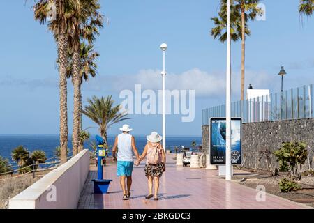 Costa Adeje, Teneriffa, Kanarische Inseln, 4. Mai 2020. Da der Covid 19, Coronavirus Notstand, die Sperrung entspannt, können ältere Menschen zwischen 10 UND 19 UHR trainieren. Ein älteres Paar geht Hand in Hand und genießt ihre neue Freiheit auf der Promenade in Fanabe. Stockfoto