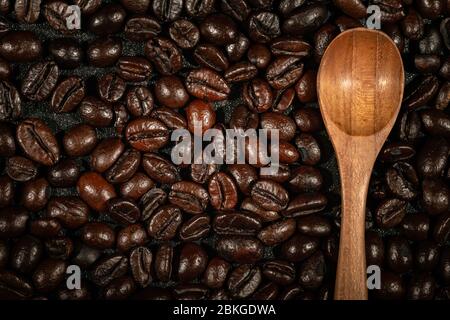 Nahaufnahme von braunen, gerösteten Kaffeebohnen mit Holzlöffel Hintergrund. Stockfoto