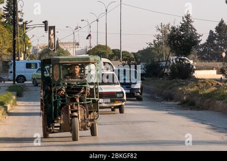 Ein Tuk-Tuk in den Straßen mit einem Porträt von Bashar Al-Assad im Hintergrund, Qamischli, Syrien. Stockfoto