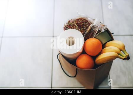 Papiertüte mit Essen und Toilettenpapier auf dem Boden am Eingang zum Haus. Covid-19 Ausbruch, Selbstisolierung, Lieferung, Spende. Stockfoto