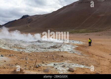 Besucher neben den dampfenden Schlammquellen im Geothermalgebiet Námafjall (auch Hverir genannt), Island. Stockfoto