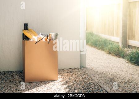 Papiertüte mit Lebensmitteln auf dem Boden neben der Hauswand. Covid-19 Ausbruch, Selbstisolierung, Lieferung, Spende. Stockfoto