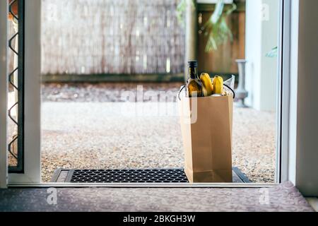 Papiertüte mit Essen und Toilettenpapier auf dem Boden am Eingang zum Haus. Covid-19 Ausbruch, Selbstisolierung, Lieferung, Spende. Stockfoto