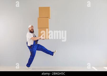 Lustige fette bärtige Lieferung Kurier Lader Mann in einer blauen Uniform mit einem Karton auf einem grauen Hintergrund. Stockfoto