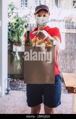 Lieferung Frau in Schutzmaske und Handschuhe liefert Papiertüte mit Lebensmitteln. Gesundheitsschutz, Sicherheit und Pandemie. Stockfoto