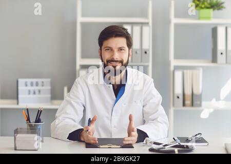 Lächelnder bärtiger Arzt, der in einem Krankenhaus sitzt. Stockfoto