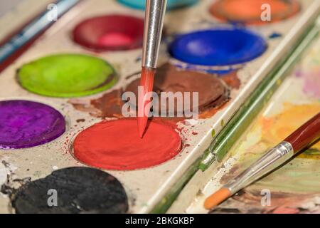 Malerpalette mit Pinsel, der in rote Aquarellfarbe getaucht wird Stockfoto