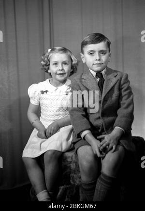 Zwei charmante Kinder posieren in den besten Kleidern eines Fotografen, aufgenommen in den frühen 1950er Jahren Stockfoto