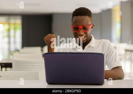Glücklich junge Afrikaner Mann als Student mit Laptop und immer gute Nachrichten in Innenräumen Stockfoto