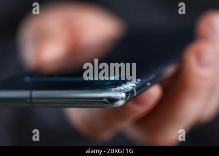 Mann hält modernes Smartphone mit gerissener Ecke in der Hand Stockfoto
