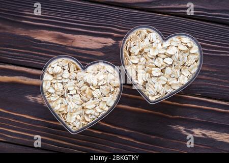 Rohe Haferflocken auf dunklem Holzbrett Hintergrund. Trocknen Sie rohe Cerealien in zwei Schüssel in Herzform Stockfoto