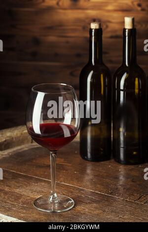 Flasche und Glas Rotwein auf Holzfass mit dunklem Holzhintergrund Stockfoto