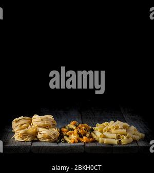 Frische Pasta in verschiedenen Formen und Farben auf einem Holz vor schwarzem Hintergrund Stockfoto