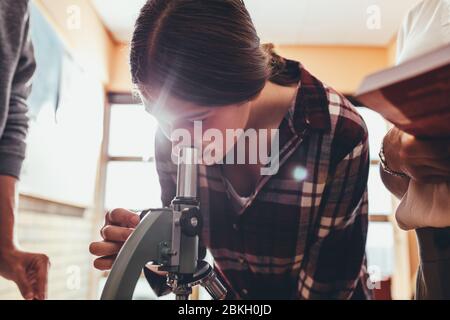 Schulmädchen in der Wissenschaft Klasse mit einem Mikroskop mit Lehrer und Klassenkamerad stehen vorbei. Student im Biologieunterricht durch Mikroskop. Stockfoto