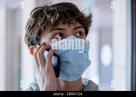 Nahaufnahme eines Teenagerjungen mit medizinischer Maske, die während des Lockdown auf dem Smartphone spricht Stockfoto