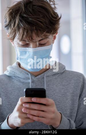 Nahaufnahme eines Teenagers mit chirurgischer Maske mit Smartphone während des Coronavirus Stockfoto