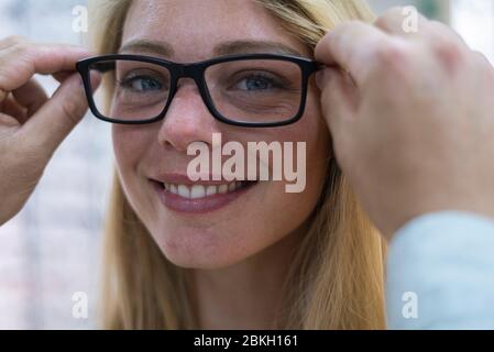 Nahaufnahme eines Verkäufers, der dem Kunden hilft, Brillen im Geschäft zu tragen Stockfoto