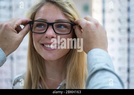 Nahaufnahme eines Verkäufers, der dem Kunden hilft, Brillen im Geschäft zu tragen Stockfoto