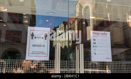 Plakate mit Covid-19-Sicherheitsvorschriften am Eingang eines Geschäfts in der Münchner Fußgängerzone (Neuhauser Straße). Mit Glas Reflexion von Häusern. Stockfoto