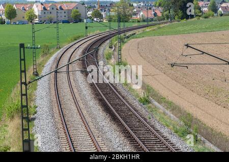 Zwei Bahngleise führen durch eine Landschaft mit grünen und braunen Feldern. Eine Stadt am Horizont. Mit Biegung / Kurve. Symbol für Reise, Reise. Stockfoto