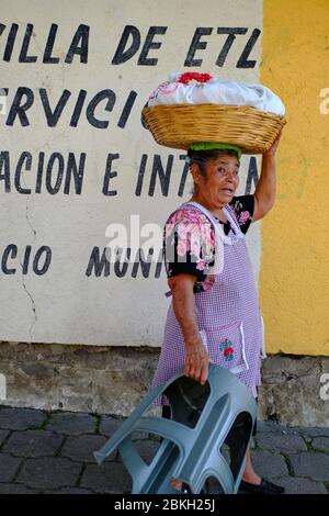Porträt eines Straßenverkäufers mittleren Alters, der einen Korb auf dem Kopf und einen Plastikstuhl in der Hand trägt. Stockfoto