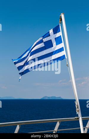 Griechische Flagge am blauen Himmel und blauer Meereshintergrund auf der achtern von einem Fährschiff. Vertikal. Stockfoto