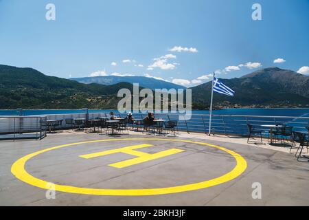 Insel Poros, Kefalonia, Griechenland - Juli, 17 2019: Gelbe Zeichen der Landeplatz für Hubschrauber an das Schiff und die Passagiere auf dem offenen Deck achtern entspannende und Stockfoto