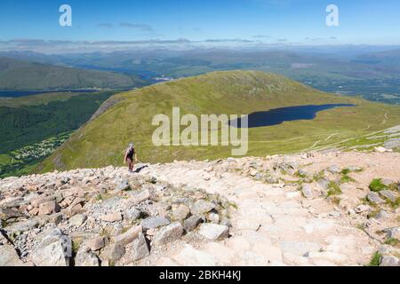 Eine Wanderin auf einem Steinpfad mit einem See (Lochan Meall an T-suidhe) im Hintergrund auf Ben Nevis, Scottish Highlands, Schottland Stockfoto