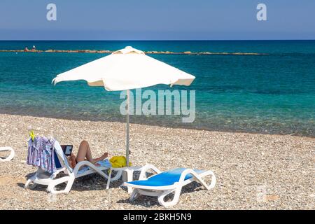 Touristen liegen auf einem Strandstuhl und lesen am Latchi Beach, Zypern Stockfoto