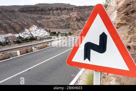 Verkehrswarnschild: Biegen Sie vor. Ein dreieckiges Straßenschild, das auf einer Straße in den Hügeln von Gran Canaria Kurven vor sich hinabführt. Stockfoto