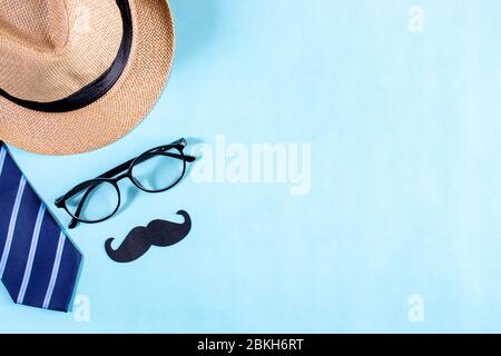 Happy Vaters Day Konzept. Draufsicht der blauen Krawatte, schöne Geschenkbox, Mann Hut mit Gläsern und Schnurrbart auf hellblau pastellfarbenen Hintergrund. Flaches Lay Stockfoto