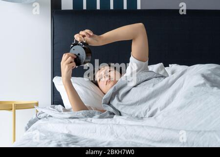 Das Mädchen schaltet den lästigen Wecker aus, um weiter zu schlafen. Holen Sie sich mehr Schlaf. Es ist ein harter Morgen. Zeit zum Aufwachen Stockfoto