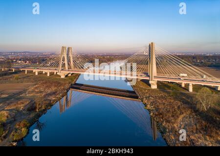 Neue moderne Doppelseilbrücke mit breiten dreispurigen Straßen über der Weichsel in Krakau, Polen, und ihre Reflexion im Wasser bei Sonnenaufgang. Stockfoto