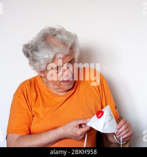 Ein Senior, der eine antivirale schützende FFP3 N99 Maske studiert, die vor Coronavirus schützt. Weißhaariger kaukasischer Mann in orange T-Shirt auf weißer Wand Stockfoto