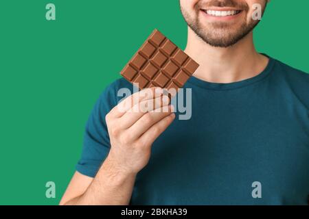 Schöner junger Mann mit leckeren Schokolade auf farbigen Hintergrund Stockfoto