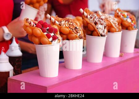 Bubble Waffeln mit Himbeeren, Schokolade und Marshmallows in white paper Cups sind auf offene Küche Food Festival verkauft. Street Food in der Garküche Stockfoto