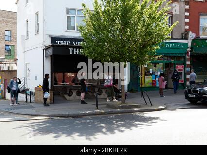 Während der COVID-19 Pandemie beobachten Menschen strenge soziale Distanzierungen, während sie sich anstellen, um das Ladywell Post Office zu betreten Stockfoto