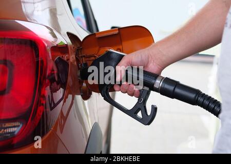 Mann füllt sein orangenes Auto mit Benzin an der Tankstelle. Tankstelle Pumpe. Zum Befüllen des Fahrzeugs mit Kraftstoff. Stockfoto