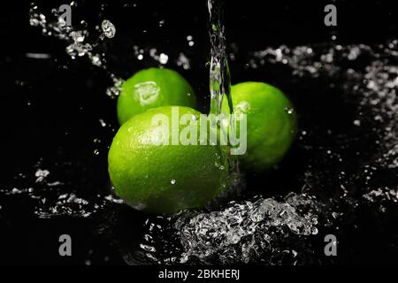 Frische Limetten mit Wasserspritzern auf dunklem Hintergrund Stockfoto