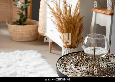 Glashalter mit Kerze und Korbmatte auf dem Tisch im Zimmer Stockfoto