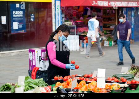 Stallhalterin im Lewisham Market, trägt eine Gesichtsmaske und inspiziert ihre Tomaten während der COVID-19 Pandemie, Lewisham High Street Stockfoto
