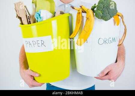 Junger Mann isoliert auf weißem Hintergrund. Schnittansicht und Nahaufnahme der Hände, die Eimer mit abgetrenntem organischen und Papierabfall für das Recycling bereit halten. Stockfoto