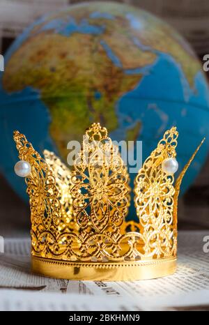 Goldene Krone mit Perlen, die Covid-19 auf Zeitungen mit Globus auf Bokeh Hintergrund darstellen. Stockfoto