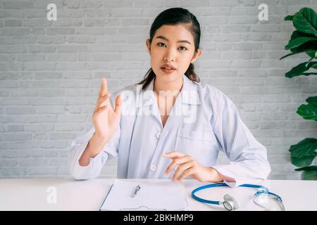 Kamera-Ansicht der Online-Videokonferenz Chat mit asiatischen Ärztin und Patientin während der Diskussion und Diagnose auf Laptop und Blick auf Kamera. Stockfoto